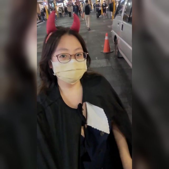 Girl in Devil Horns Flashes on a Busy Street at Halloween